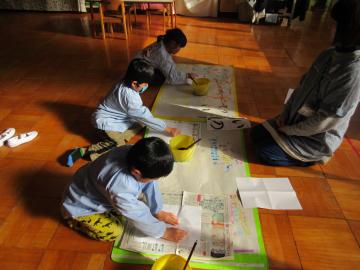 新聞紙が敷かれた床の上で園児たちが書初めをしている写真