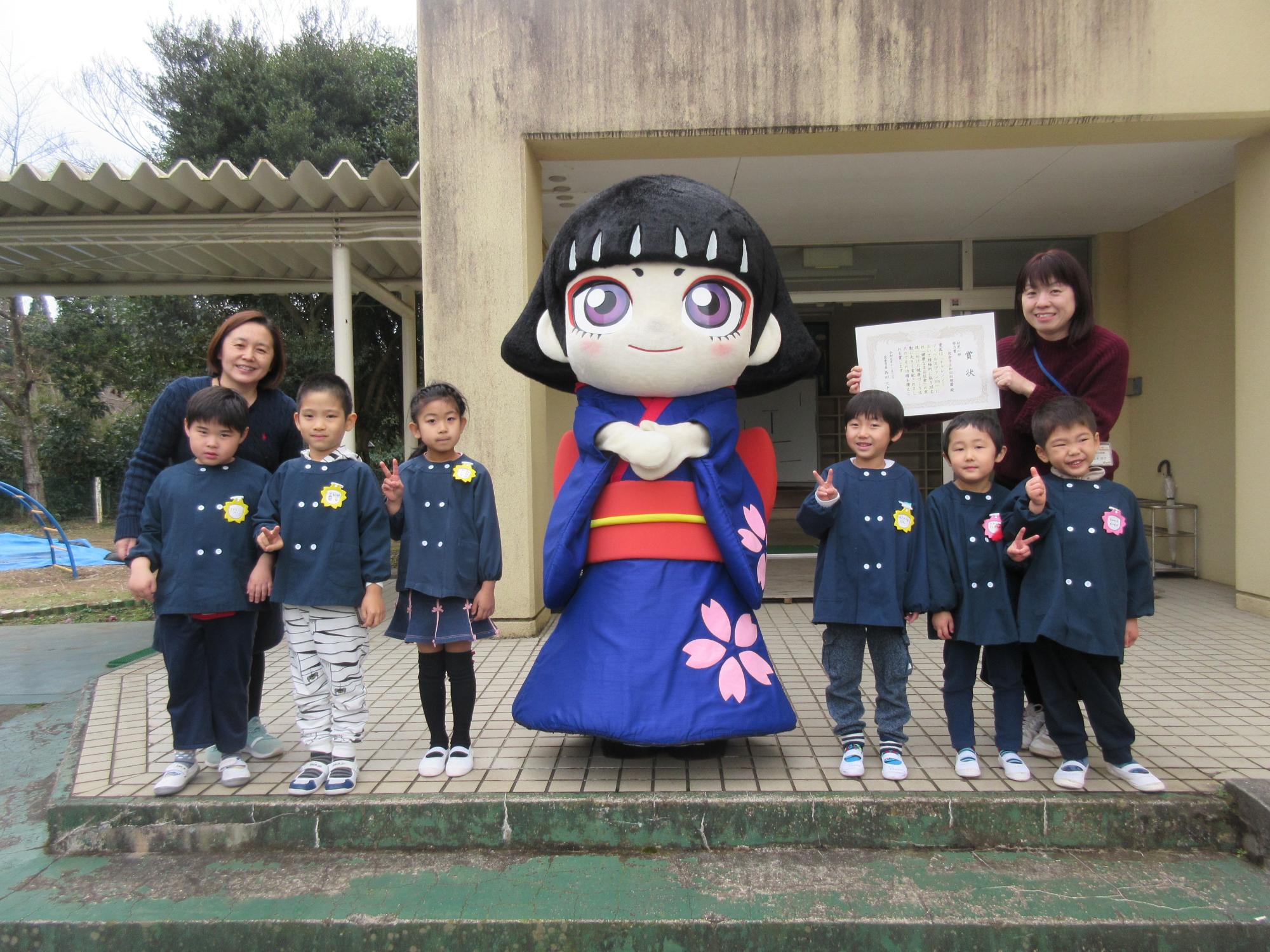 カムロちゃんの着ぐるみとピースをした園児たちが並んでいる記念写真