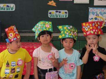 4名の年少組の子ども達が、色画用紙で作ったこいのぼりを頭に被って黒板の前に横一列に立ってピースサインをしている写真