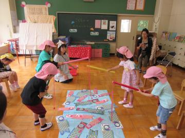 手作りの鯉のぼりを大きな水色の紙の上に置いて、ピンク色の帽子を被った子供たちが釣り竿の紐から紐を垂らして、魚つりゲームをしている様子の写真