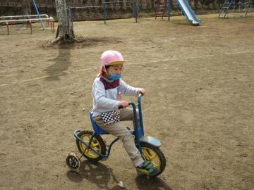 一人の園児がマスクをして三輪車に乗っている写真