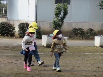 マスクをして黄色い帽子を被った園児たちが園庭を歩いている写真