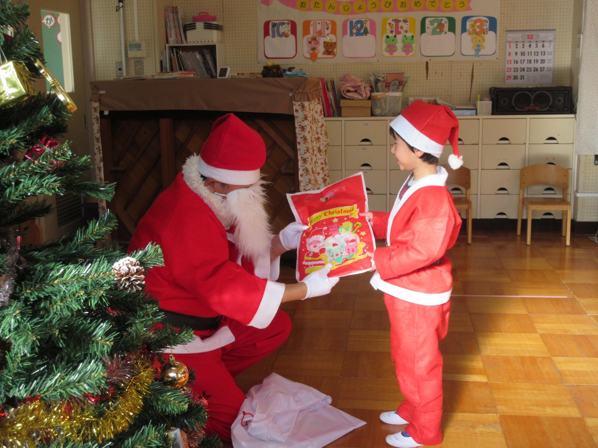 サンタクロースから、プレゼントを受け取るサンタクロースの衣装を着た園児の写真