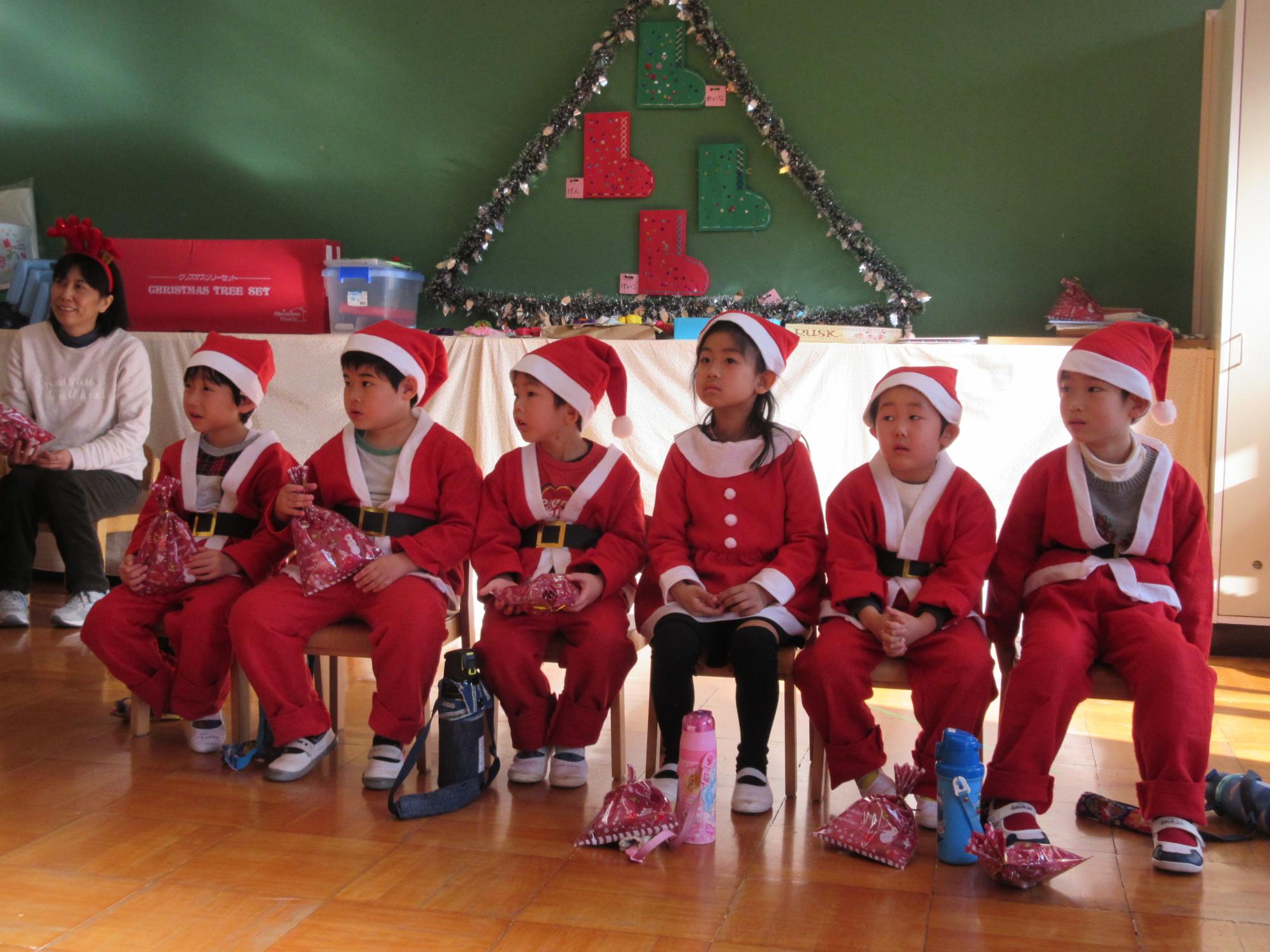 サンタクロースの衣装を着た園児6名が、プレゼントを持って着席している写真