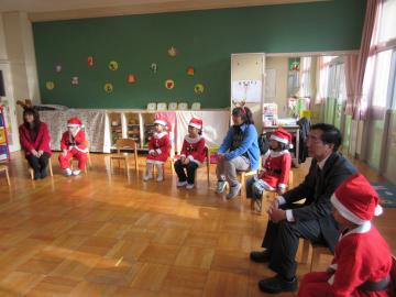 椅子が円を描くように置かれていて、サンタの恰好をした園児たちが椅子に座っている写真