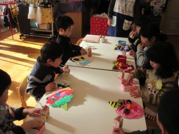 テーブルの上に子供達が作ったお面が置かれ、園児たちが座って豆を食べている写真