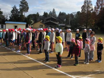 運動場に白線が引かれ、帽子を被った園児たち、小学生たちが並んでいる写真