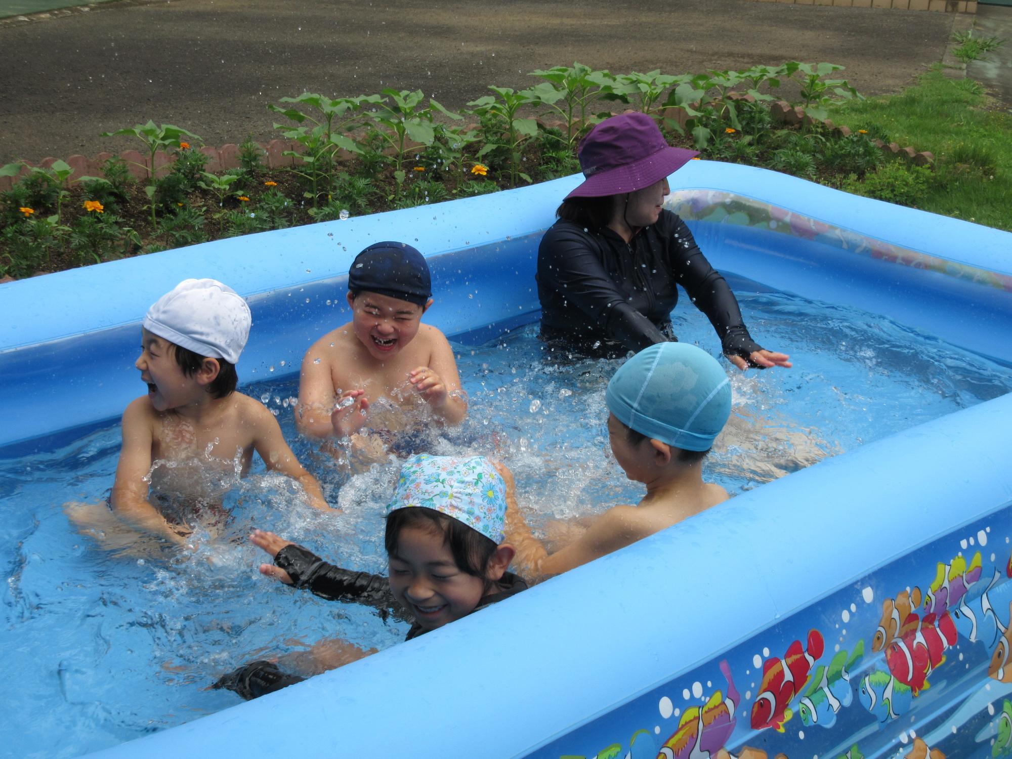 プールの中で年長組の園児4人が遊んでいて、水しぶきが上がっている写真