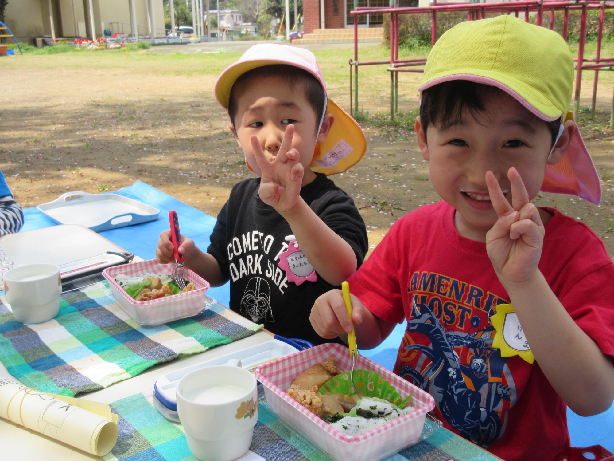 お弁当を食べる男の子の園児2名がピースサインをしている写真
