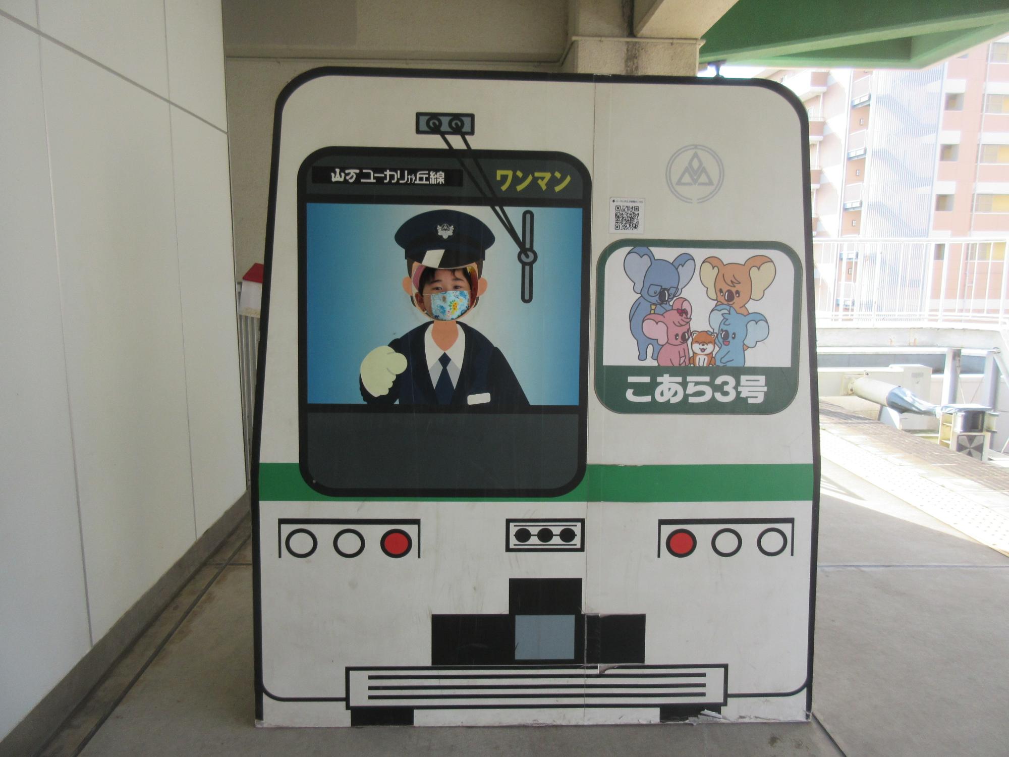 電車の運転席が描かれている顔部分がくり抜かれている顔出しパネルに園児が顔を出している写真