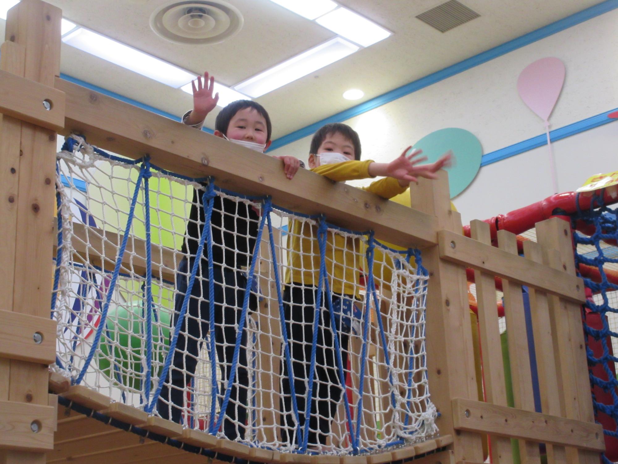 網と木で出来たつり橋のような遊具の上から園児2名が顔を出している写真