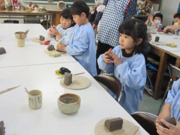 園児たちがスモックを着て、粘土をこねてお皿作りをしている写真