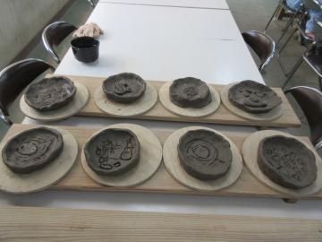 粘土で丸く作られ絵が彫られたお皿が8枚並んでいる写真