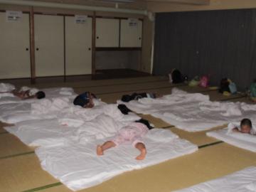様々な格好の園児が、畳の部屋の布団の上に寝ている写真