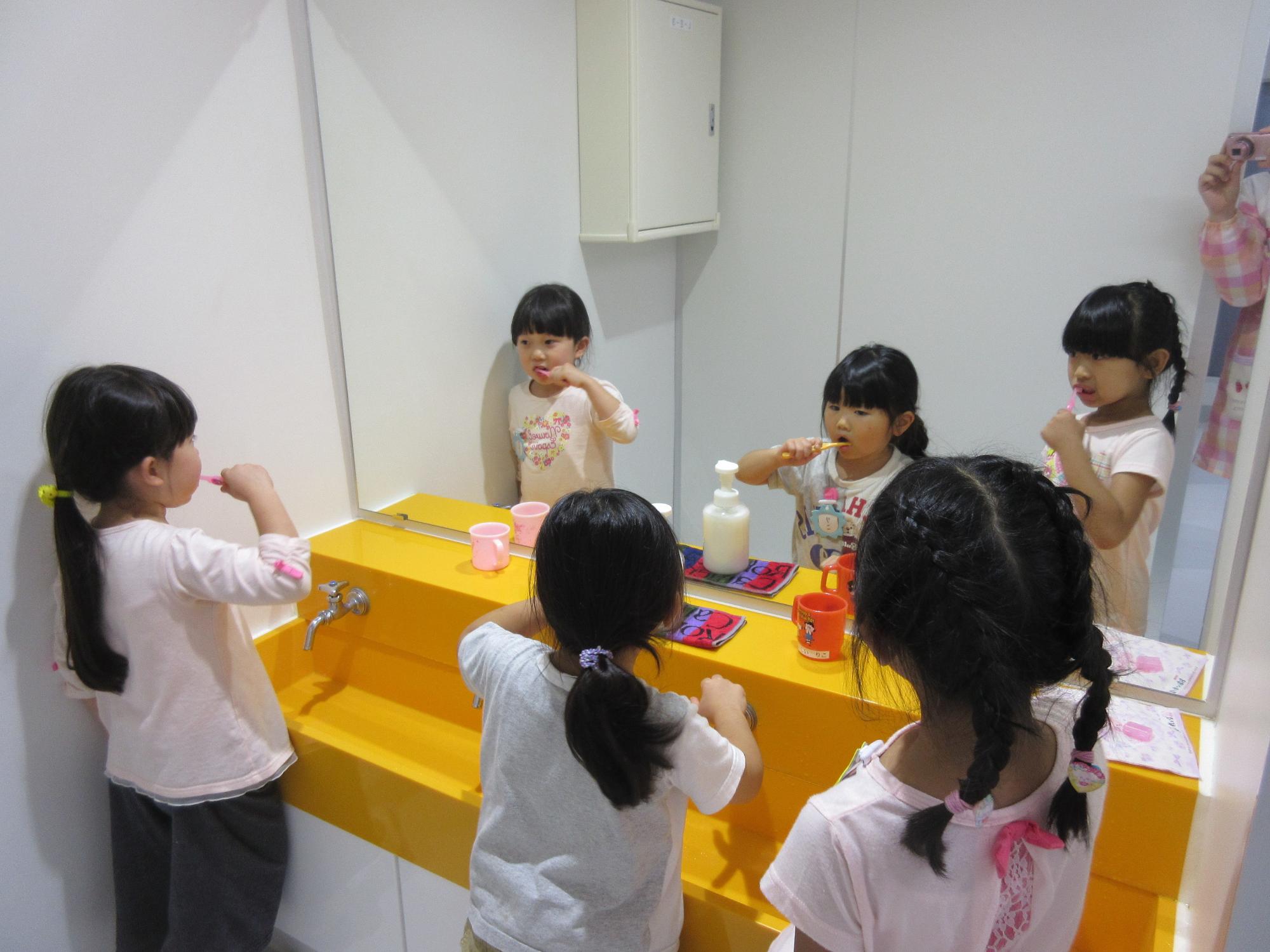 洗面台の鏡の前で園児たちが歯磨きをしている写真