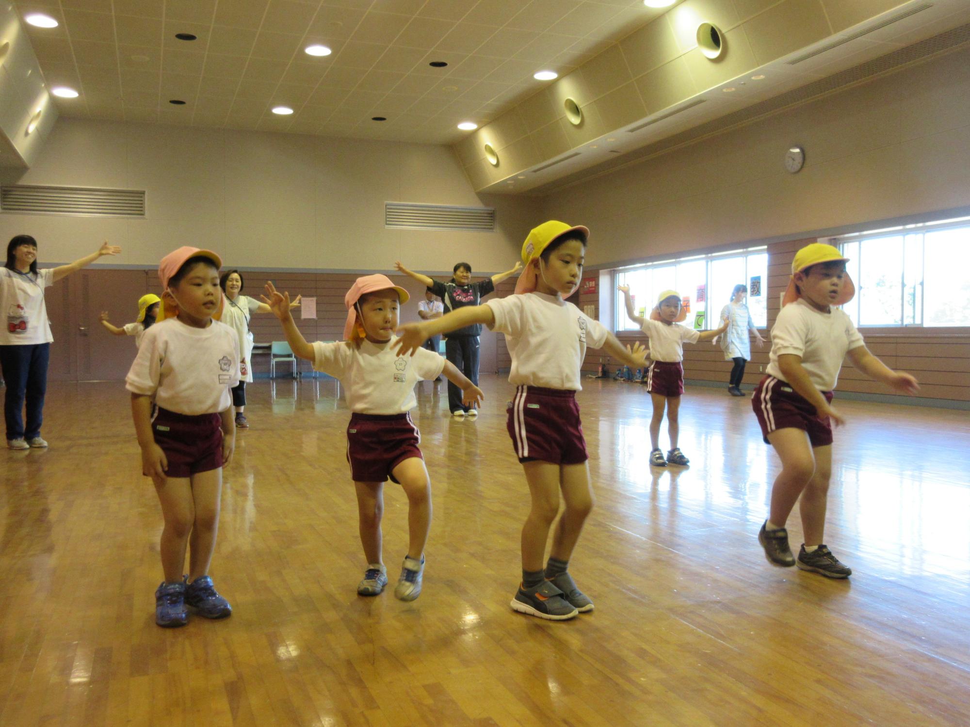 体育着を着た園児たちが両手を広げたりしながら踊りを踊っている写真