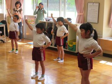 体操着を着た年長組の子ども達が間隔をあけて立ち、右手を挙げて準備体操をしている写真