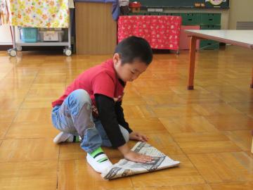 教室の床に座っている男の子が、新聞紙でかぶとを制作している写真