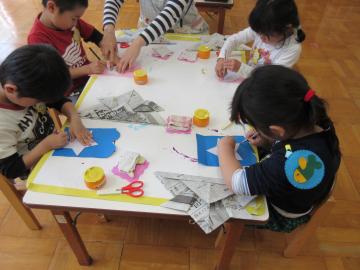 1つの机に4名の子ども達が座り、はさみや糊を使ってかぶとにつける飾りを作っている写真