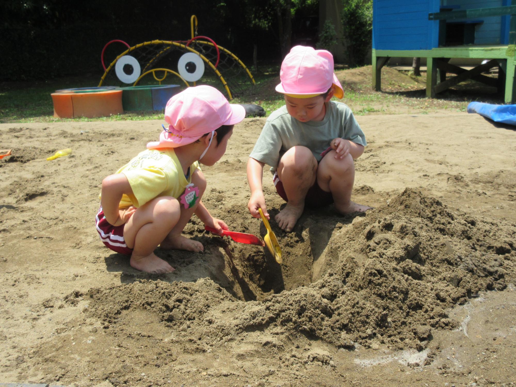 園児2人がシャベルを持って砂場の土を掘っている写真