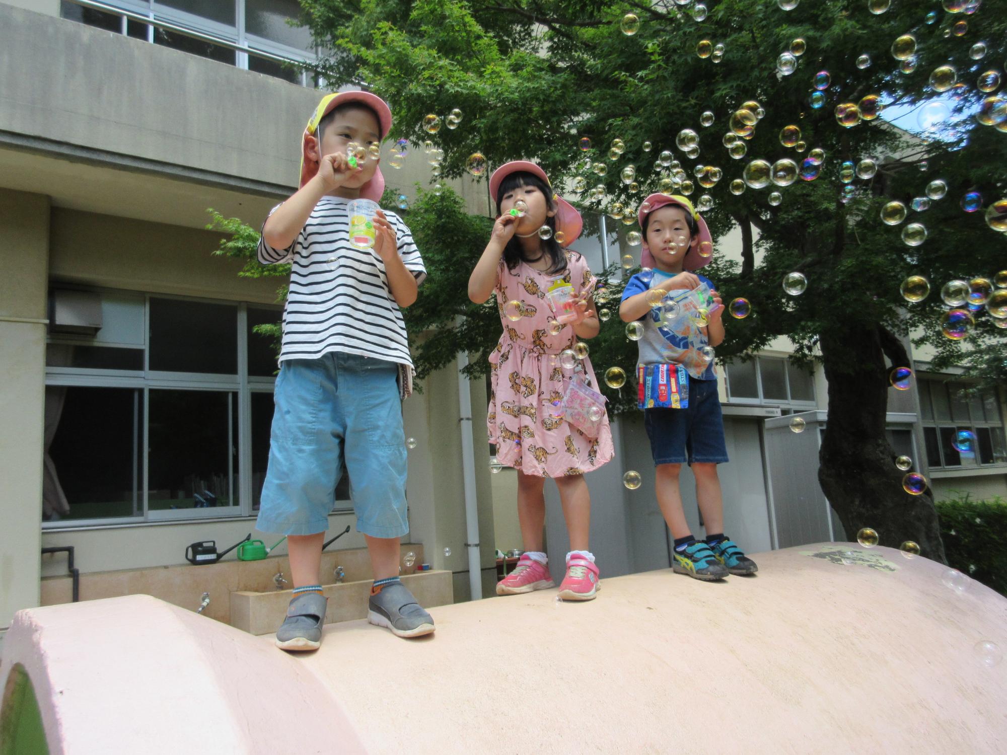 園児3人がシャボン玉を吹き、沢山の丸いシャボン玉が浮かんでいる写真