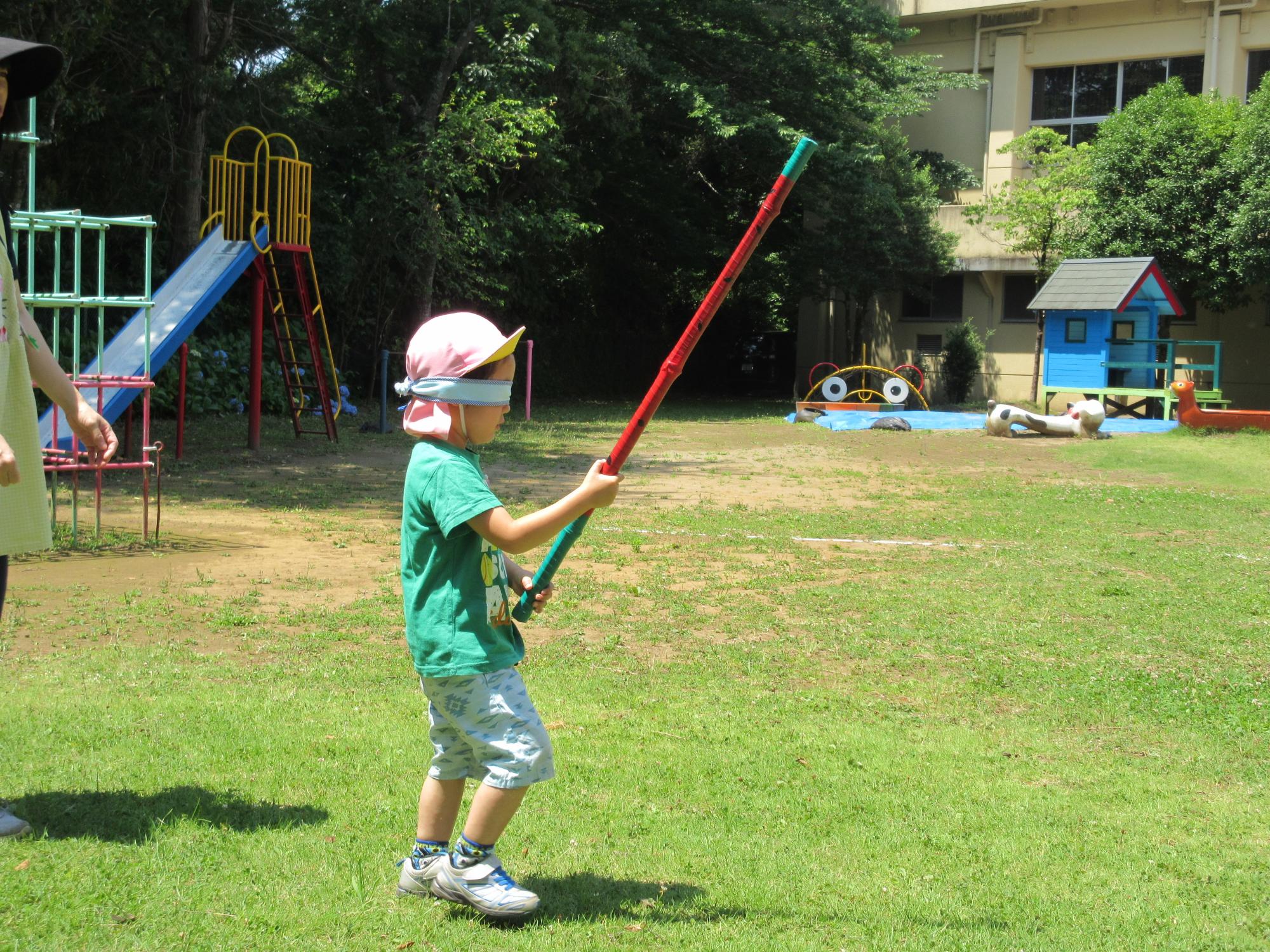 緑のTシャツを着た園児が目隠しをして棒を持ち歩いている写真