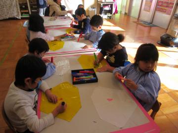 園児たちが机の上にカラーポリ袋を置いて、サインペンで絵を描いている写真