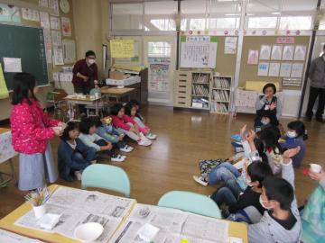 教室で園児と小学生たちがそれぞれ向かい合って座っていて、小学生数名が手を挙げている写真