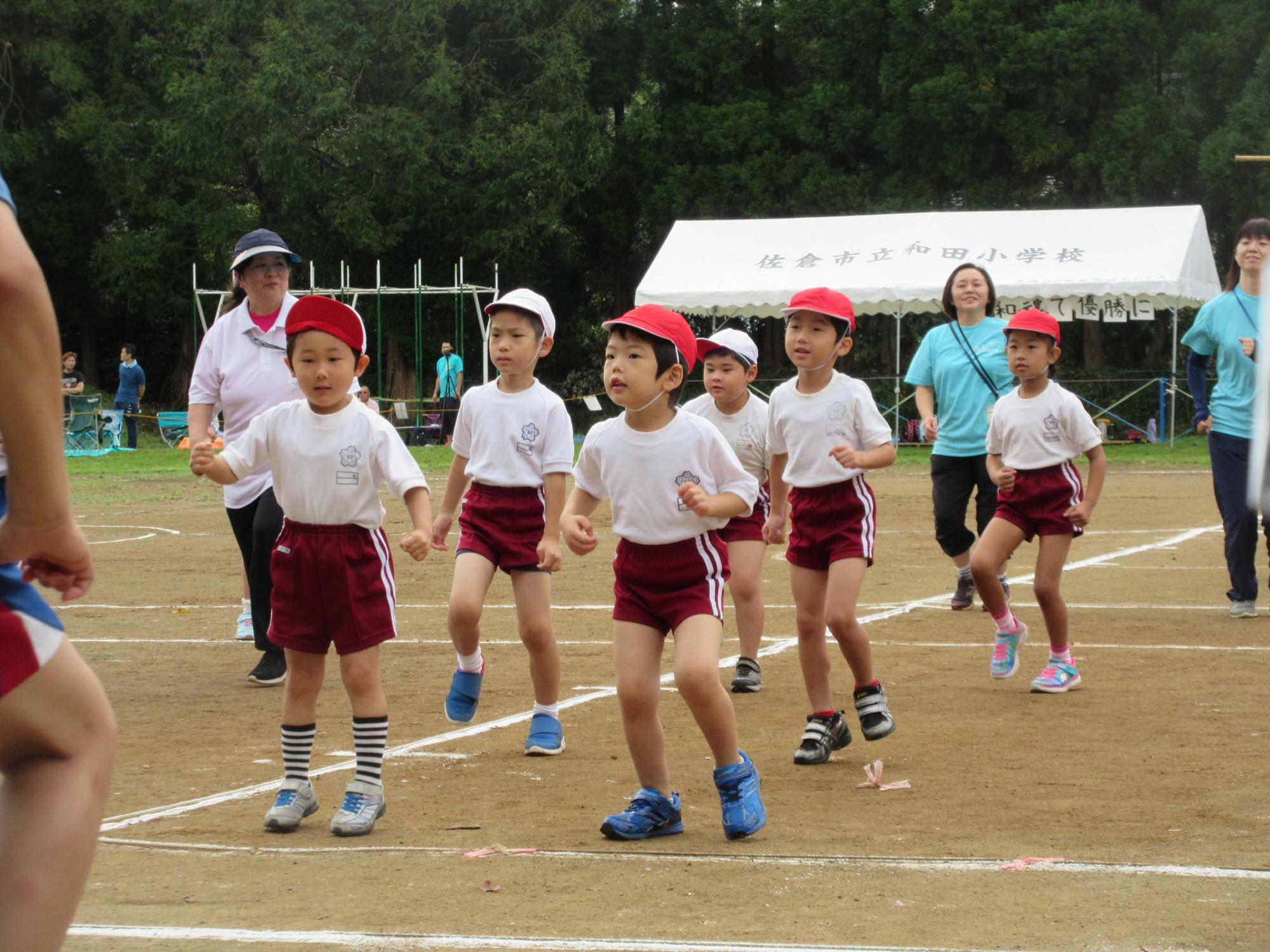 運動場で体育着を着た園児たちが並んで片足を上げている写真