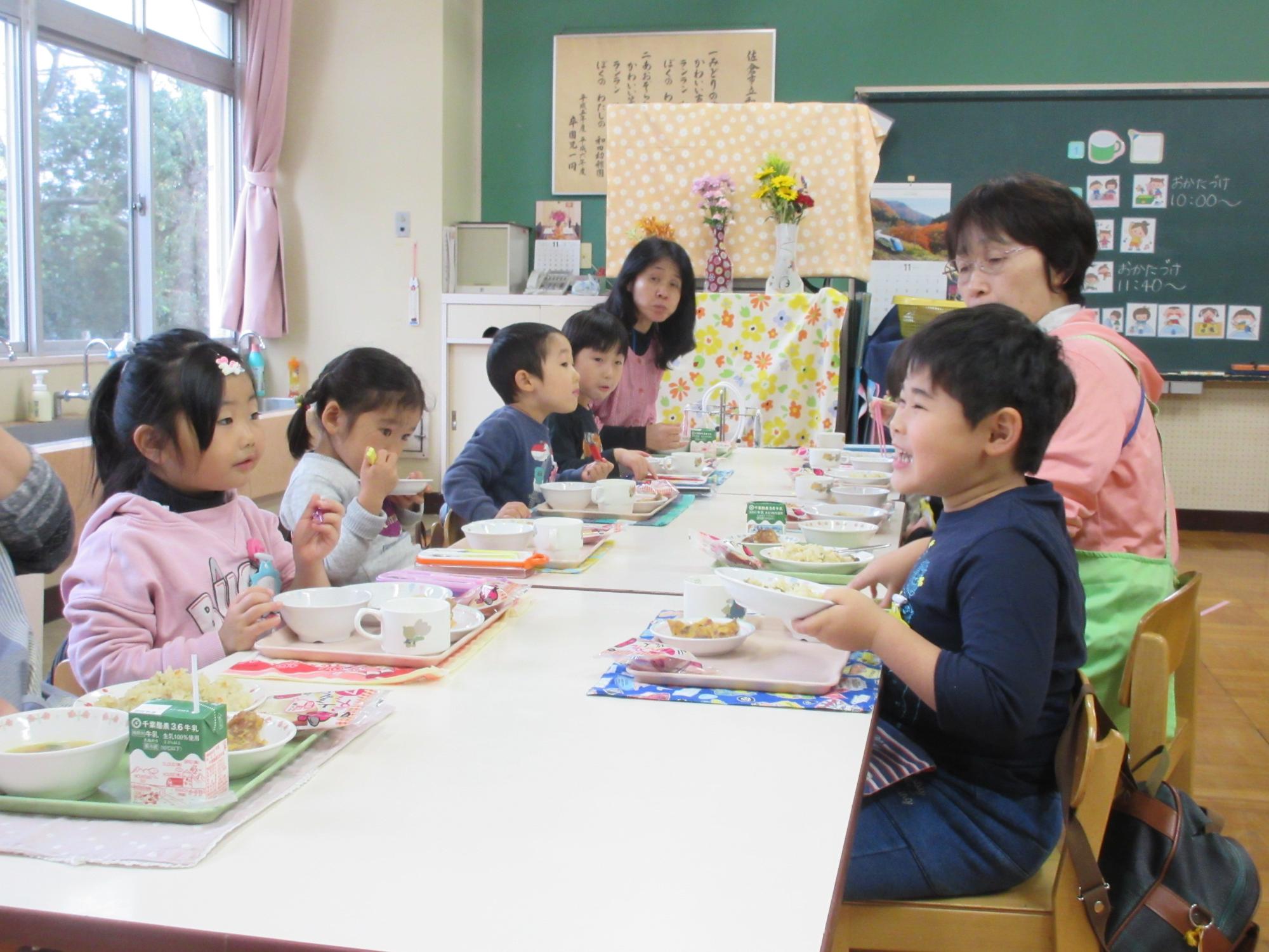 白いテーブルに園児と先生が向かい合って座り給食を食べている写真