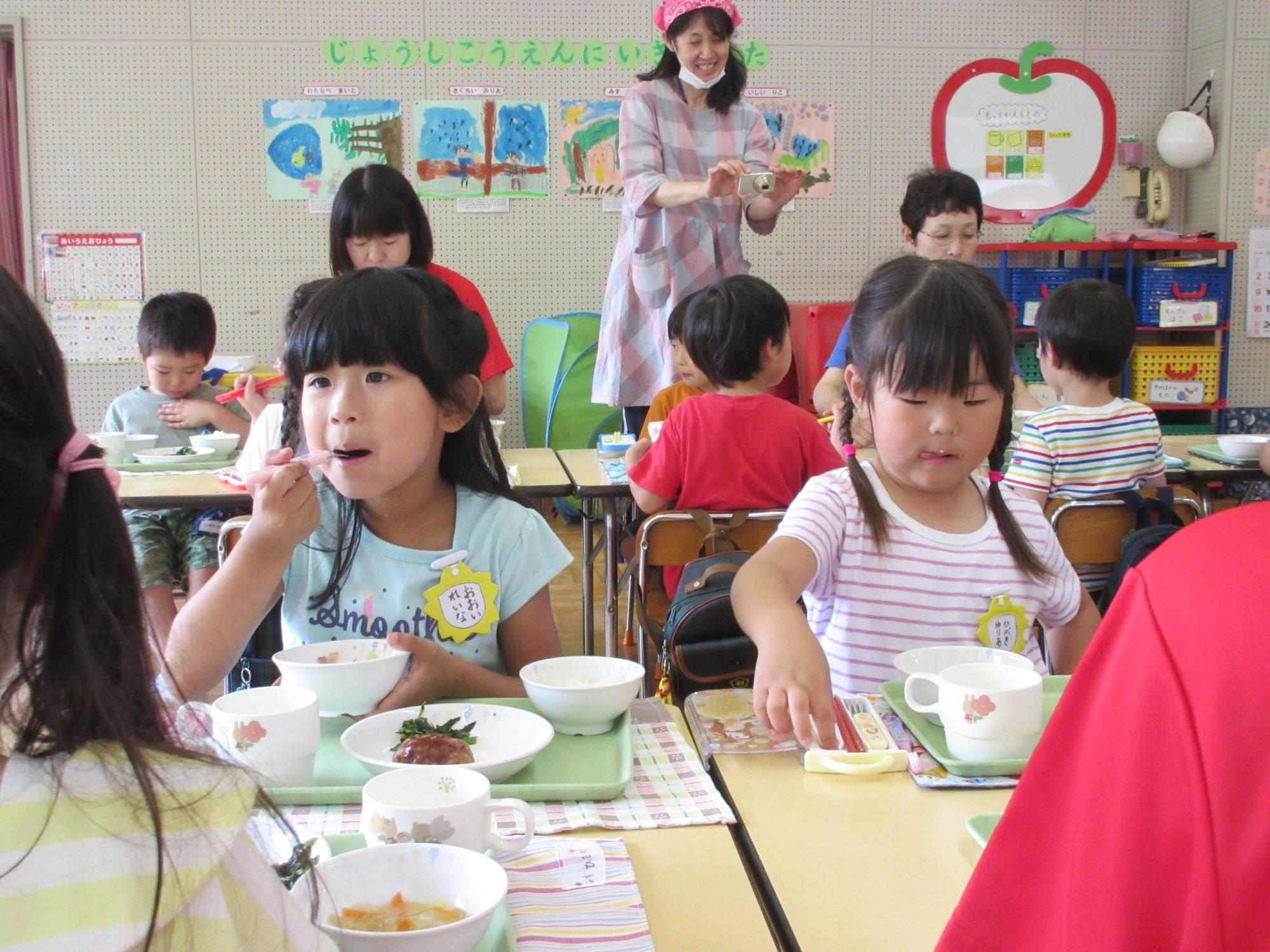 園児たちがハンバーグやスープなどの給食を食べている写真