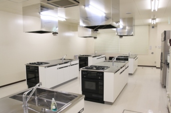 白を基調とした3台の調理台が5つ並んでいる調理室の写真