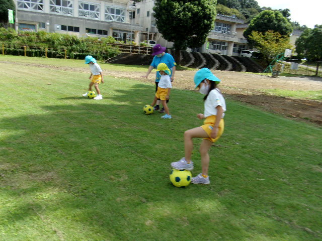サッカーボールの上に足を置いたり、蹴ったりしている3人の園児の写真