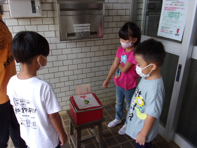 手紙が入った赤い郵便缶の前に集まっている3名の園児の写真