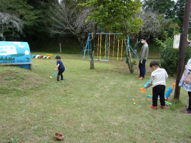 芝生の上でちいさなゴルフクラブのおもちゃを使ってパターゴルフをする子供たちの写真