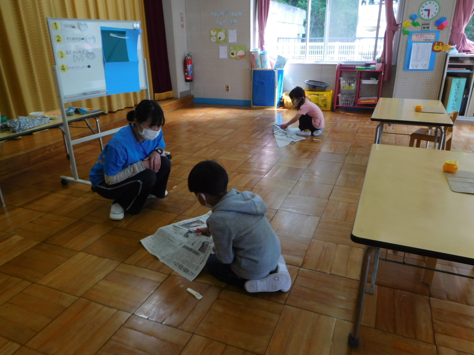 床で、男の子と女の子の園児が新聞紙を折っている写真