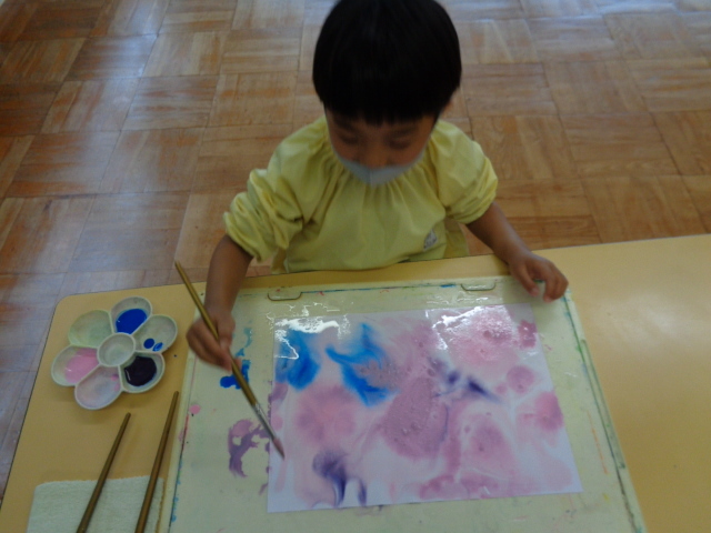 黄色いスモックを着た男の子の園児が、画用紙に色を塗っている写真