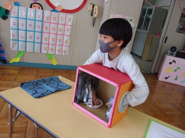 男の子の園児が、箱の中委が見えない位置に立ち、穴の中から手を入れ中に入っているものを触っている写真