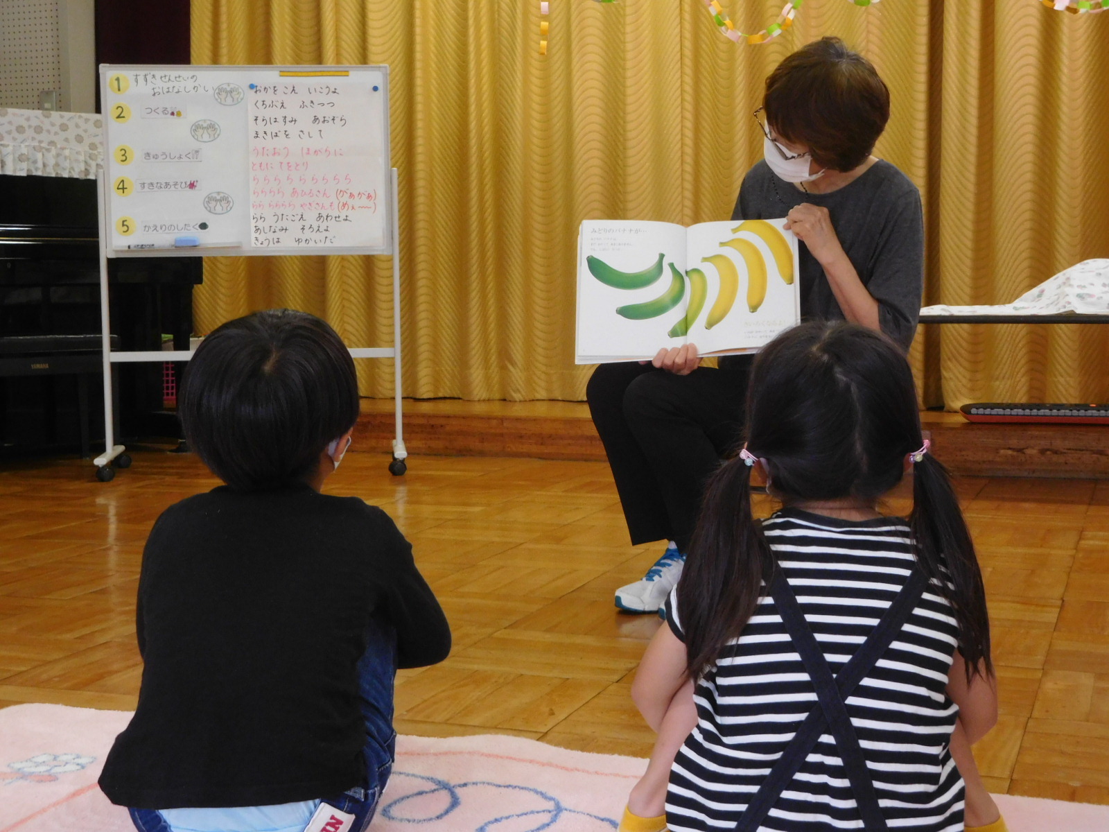司書の先生が、男の子と女の子の園児に絵本の読み聞かせをしている写真
