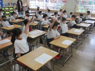 教室内で椅子に座っている1年生達が手を上げている写真
