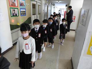 マスク姿で一列に並んで廊下を歩いている新1年生たちの写真