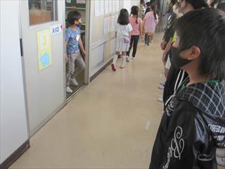 1年生達が教室から廊下へ出て歩いている様子を廊下に並んでみている6年生たちの写真