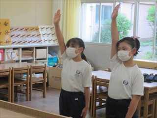 教室内で体操着姿でマスクを付けたまま選手宣誓をしている2人の女子生徒の写真