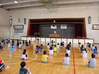 2年生が間隔を置いて体育館に集まって座って前期の終業式に参加している写真