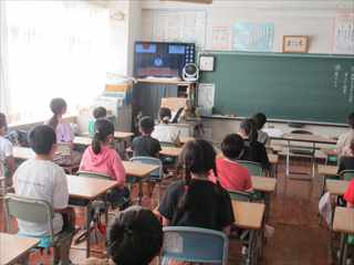各々の児童が教室の自分の席に座って黒板脇のテレビモニターを視聴している写真