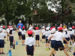 赤や白の帽子を被った子どもたちが校庭に集まって準備体操をしている写真