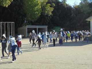シルバーの防災頭巾を被って列になって歩いている子どもたちの写真