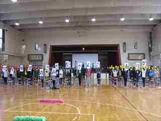 体育館で子どもたちが「6年生のみなさんありがとう」と書かれた紙を持ち並んで立っている様子の写真