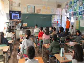 教室の左脇に設置されたモニターの映像を集中した様子で見ている子どもたちの写真