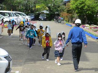銀色の防災頭巾とマスクをつけて並んで外へ出てきた生徒たちと白いヘルメットを被って引率している教師の写真